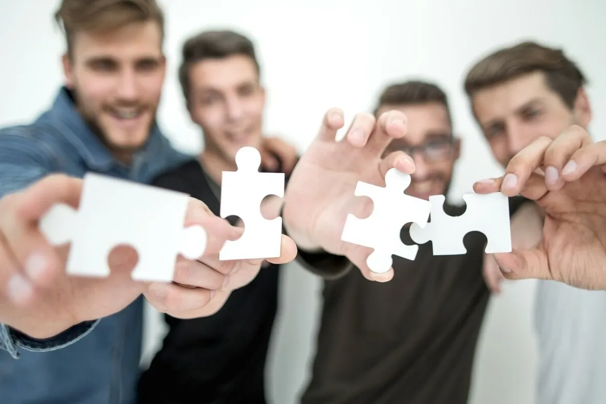 Eine Gruppe junger Männer halten jeweils ein weißes Puzzleteil ins Bild.