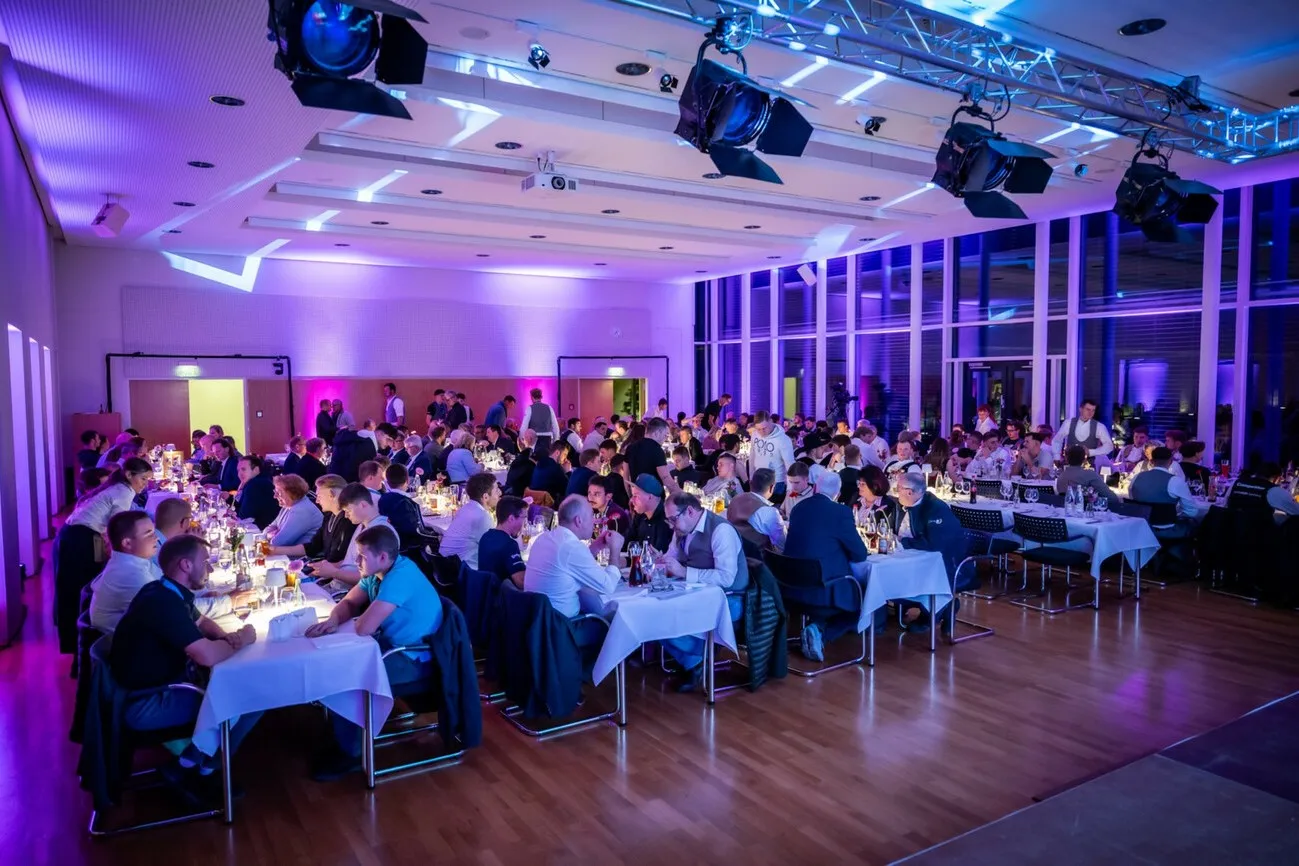 Eine Halle mit mehreren Gästen an Tischen, bläuliches Licht.