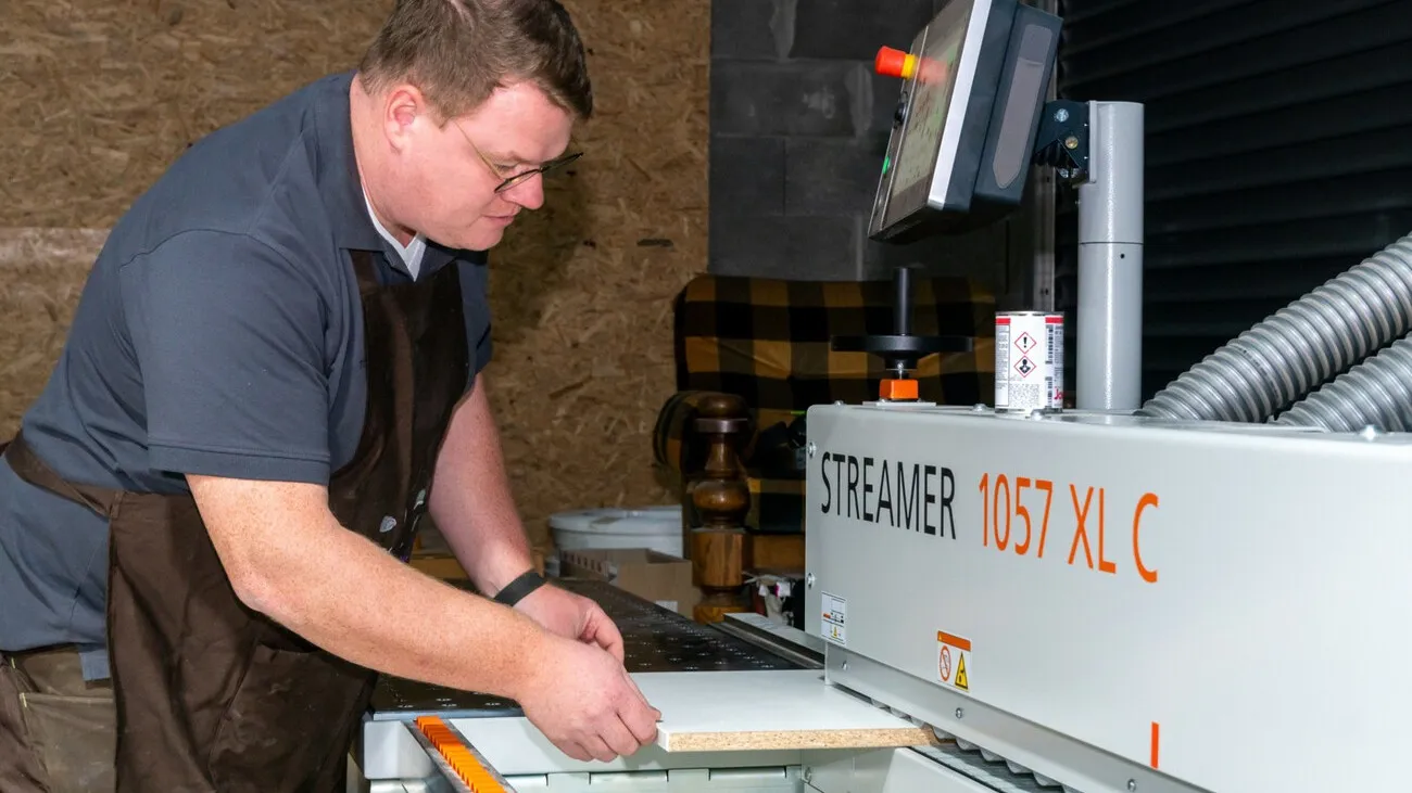 Tim Langer macht mithilfe einer Maschine eine Kunststoffkante an die Platte dran.