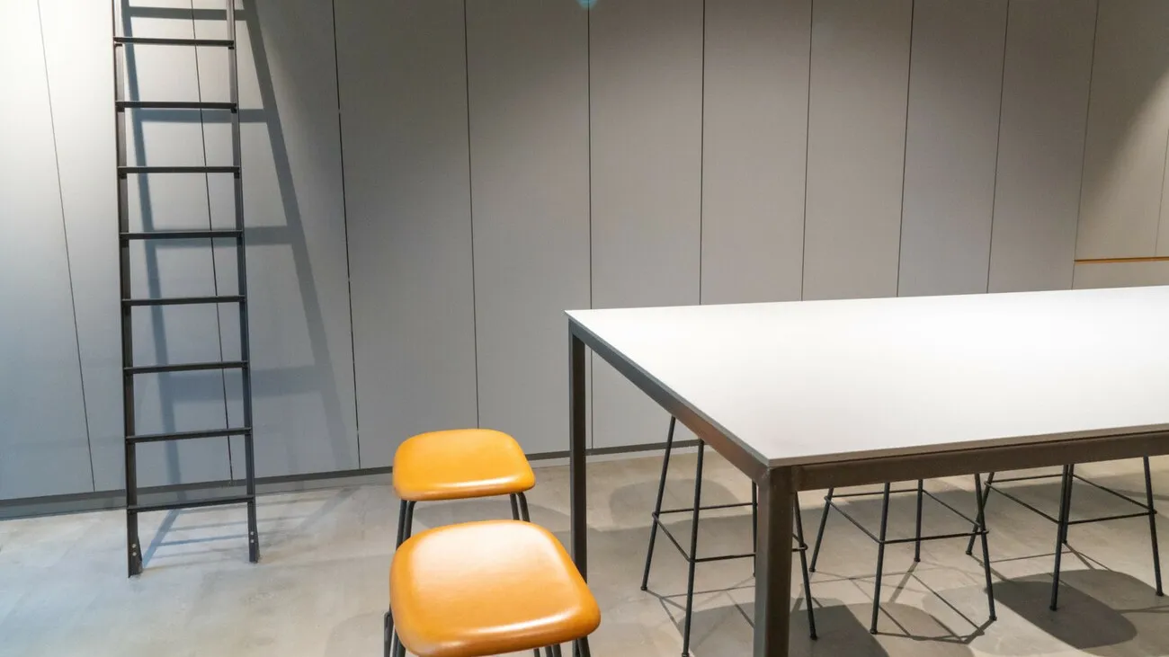 Ein Raum mit grauen Wänden und einem Tisch in der Mitte. Neben dem Tisch steht ein orangener Stuhl.