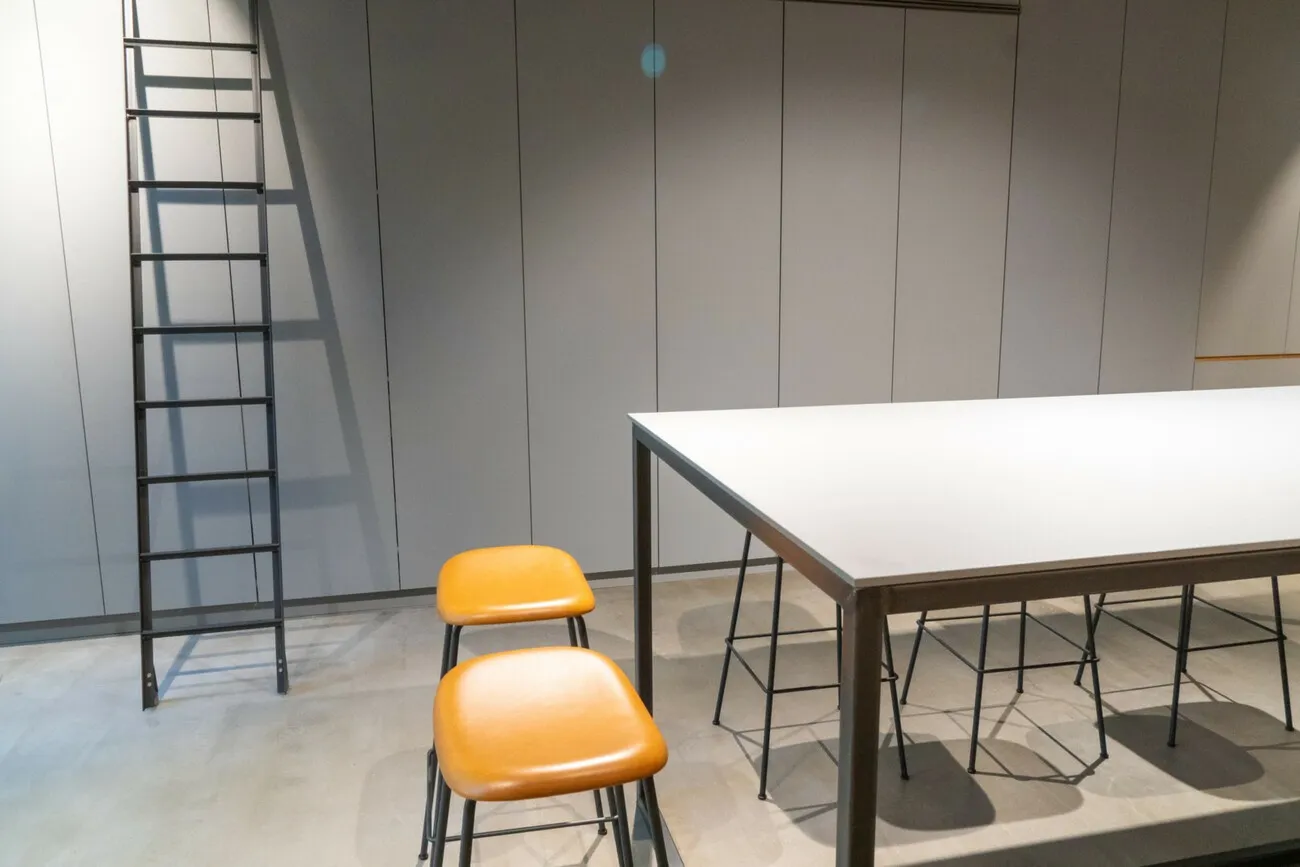 Ein Raum mit grauen Wänden und einem Tisch in der Mitte. Neben dem Tisch steht ein orangener Stuhl.