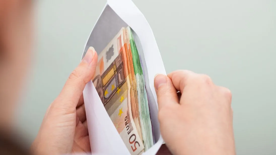 Eine Frau schaut in einen Briefumschlag, in dem diverse Euro-Noten enthalten sind.