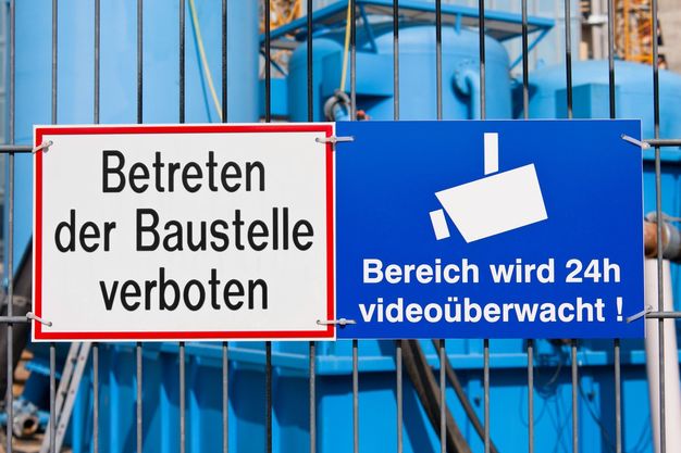 Schild am Bauzaun weist über permanente Videoüberwachung der Baustelle hin