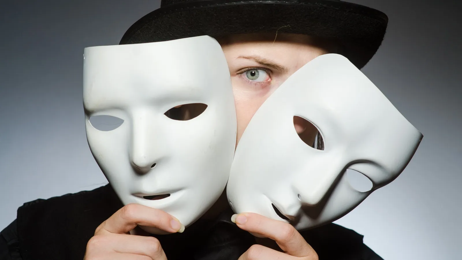 Eine Frau in schwarzer Aufmachung hält sich zwei weiße "Anonymous"-Masken vors Gesicht.