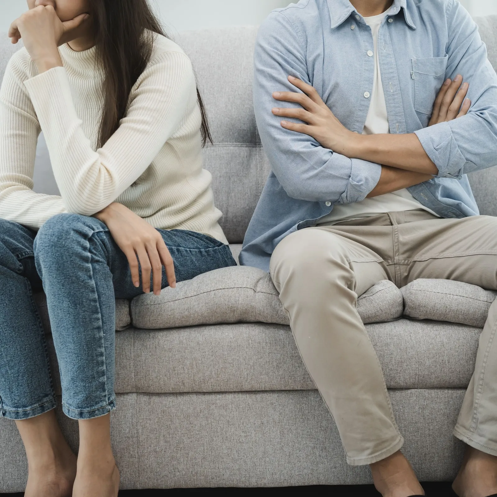 Paar sitzt zusammen auf dem Sofa, die Körper von Mann und Frau sind aber voneinander abgewand.