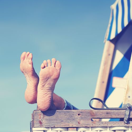 Jemand liegt im Strandkorb und legt die Füße auf die Lehne.