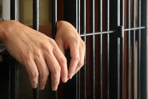 prisoner behind bars.hand of prisoner on steel jail bars.Man under arrested by policeman because illegal behaviour.