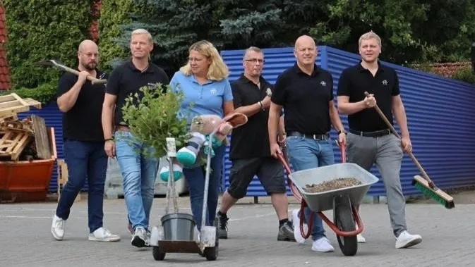 Sechs Mitarbeitende von Weber & Reil gehen gemeinsam nebeneinander her. Eine Frau schiebt einen Wagen mit einer Topfpflanze, ein Mann daneben eine Schubkarre mit Erde.