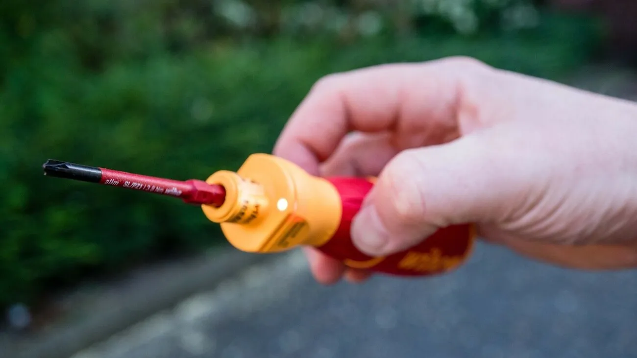 Eine Hand hält den rot-gelben E-Schraubendreher in die Kamera.