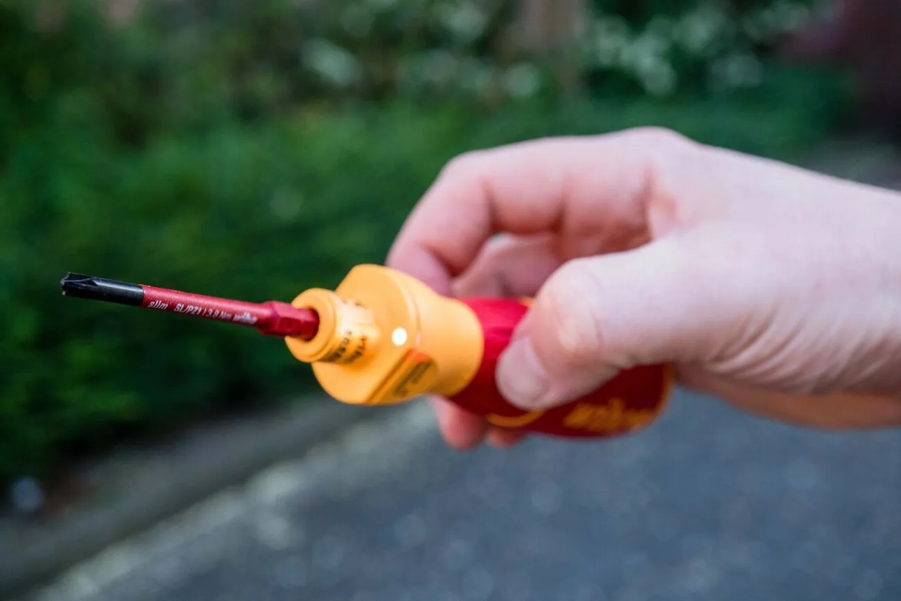 Eine Hand hält den rot-gelben E-Schraubendreher in die Kamera.
