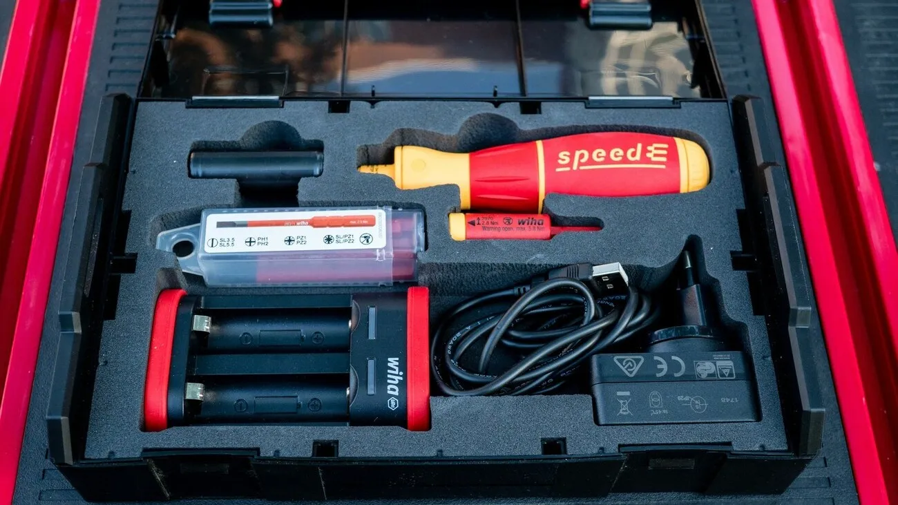 Der E-Schraubendreher in rot-gelb liegt in einem schwarzen Koffer mit weiterem Zubehör.