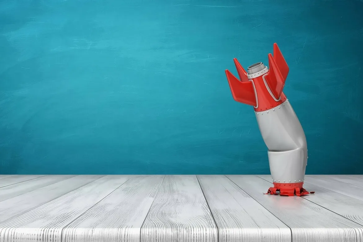 3d rendering of a red and silver realistic model of a retro rocket stands crashed into a wooden desk on a blue background. Failed launch. Technological progress. Technical mistake.