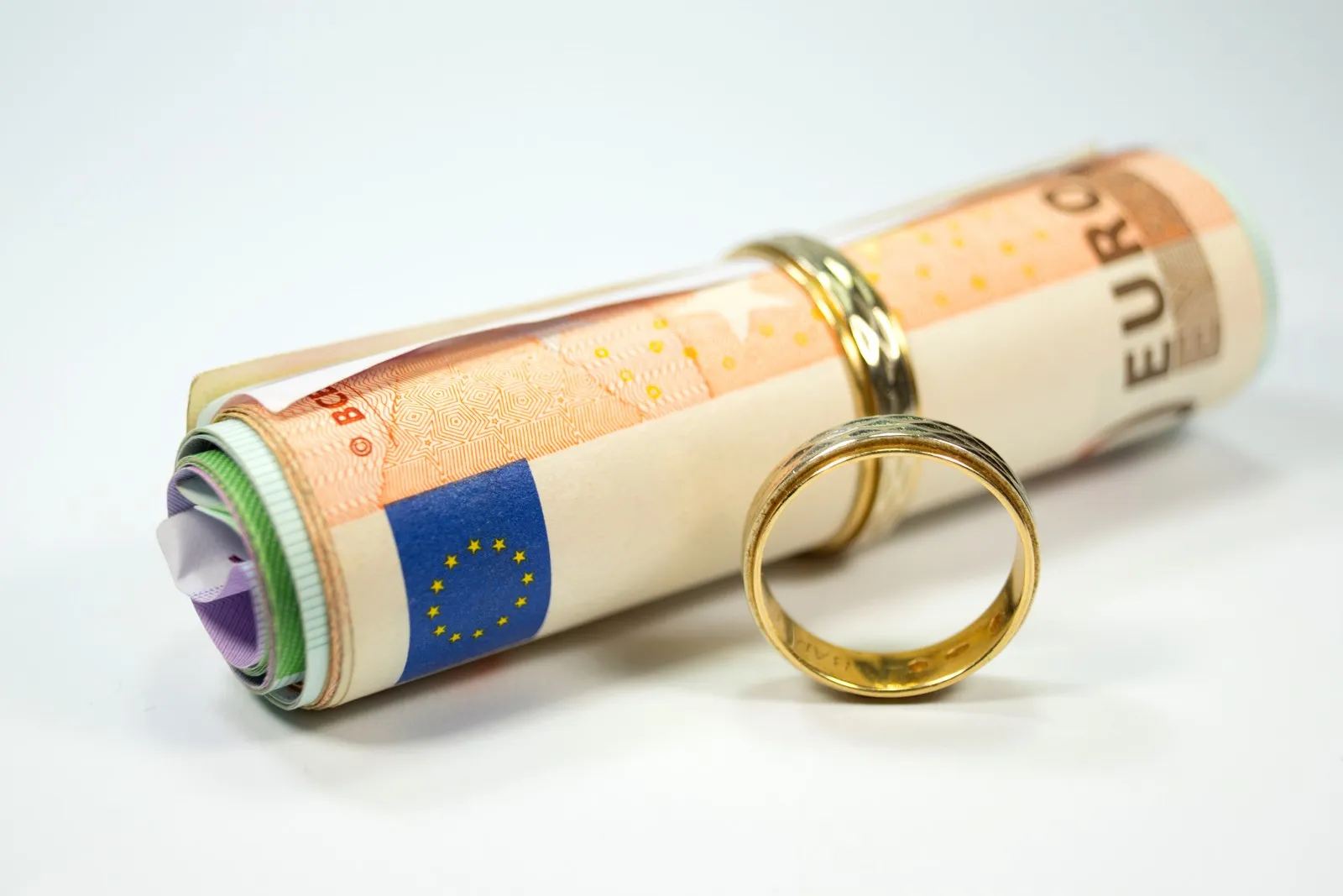 Ein Bündel Euro Scheine steckt in einem goldenen Ring, daneben liegt ein weiterer goldener Ring.
